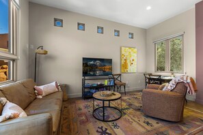 A living room with a sofa, armchair, TV, bookshelf, and a patterned rug.