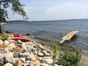 A rocky shoreline with a wooden dock extending into calm water, surrounded by large rocks and sparse vegetation. - Lakefront, private beach, dock, kayaks, Paddle Boat and pet friendly! (Plattsburgh)