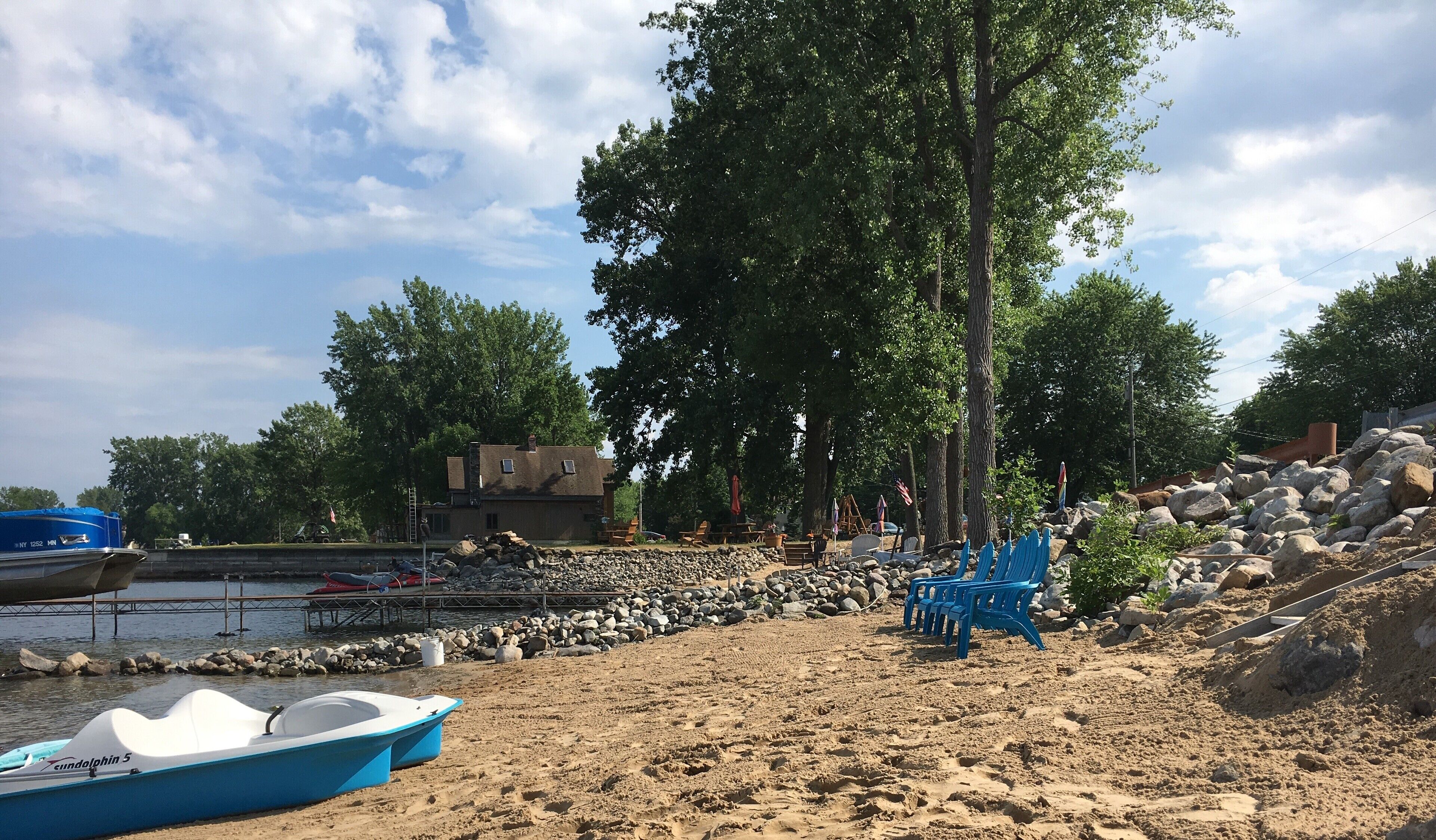 A beach with a row of blue chairs, a boat, and a rocky shoreline.