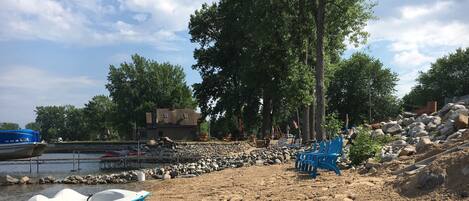 A beach with a row of blue chairs, a boat, and a rocky shoreline.