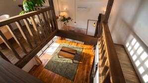 A spacious loft with a high ceiling, wooden beams, a green area rug, and a view of the city through large windows. - Yufuin Tsukahara Villa ERINA (Yufu)