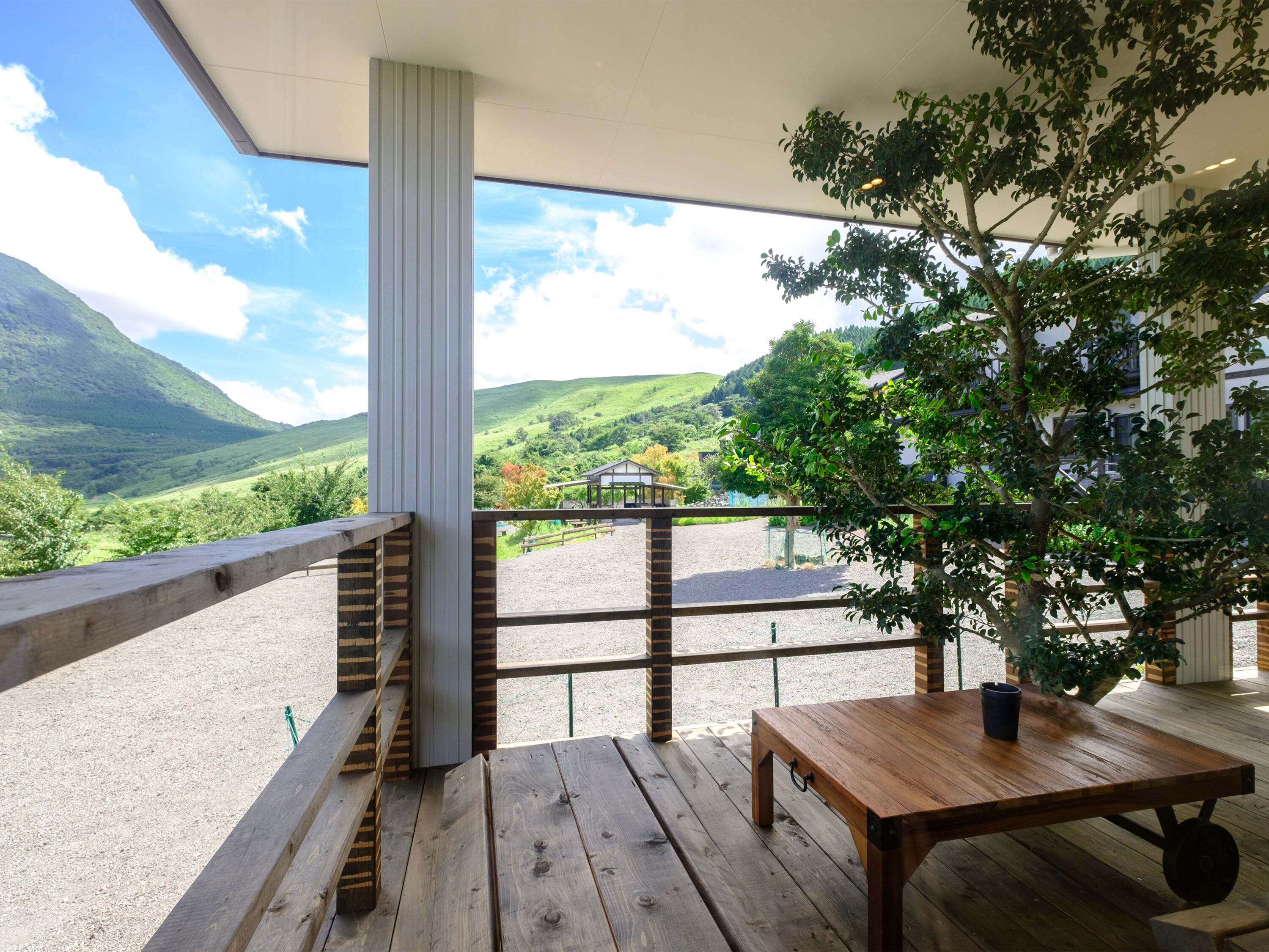 A wooden deck with a table and benches, overlooking a scenic valley with hills and a building in the distance.