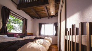 A bedroom with a wooden ceiling, a large bed with white bedding, a window with curtains, and a wooden panel wall. - Yufuin Tsukahara Villa ERINA (Yufu)