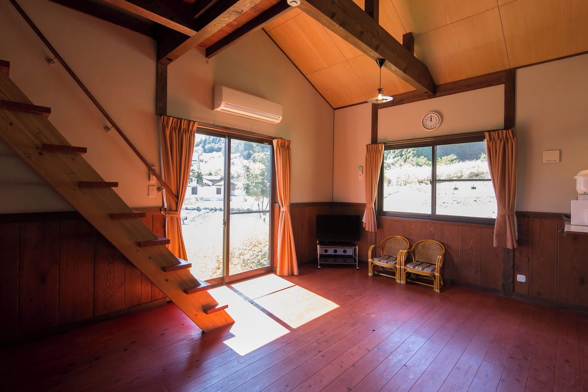 Een kamer met een houten trap, een flatscreen televisie en een zithoek met stoelen.