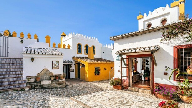 A courtyard with cobblestone flooring, a yellow building, and a white building with a red door. - Beautiful House with Private Pool near the Costa del Sol (Alcaucín)