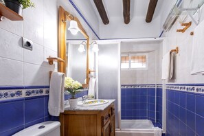 A bathroom with a white toilet, a wooden vanity with a mirror, and a shower area with blue tiles. - Beautiful House with Private Pool near the Costa del Sol (Alcaucín)