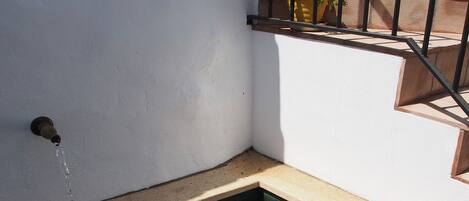 Ein kleiner, klarer Pool mit einem Wasserspeier links, einem Blumentopf rechts und einer Treppe, die zu einer erhöhten Ebene führt.