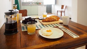 Ein Frühstückstisch mit einer French Press, einer Schale Kirschen, einem Glas Orangensaft, einem Teller mit einem Spiegelei, einem Brotlaib und einer Tasse.