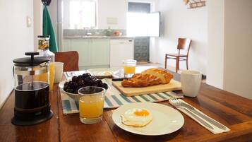 Une table de petit-déjeuner avec une cafetière à piston, un bol de cerises, un verre de jus d’orange, une assiette avec un œuf au plat, une miche de pain et une tasse.