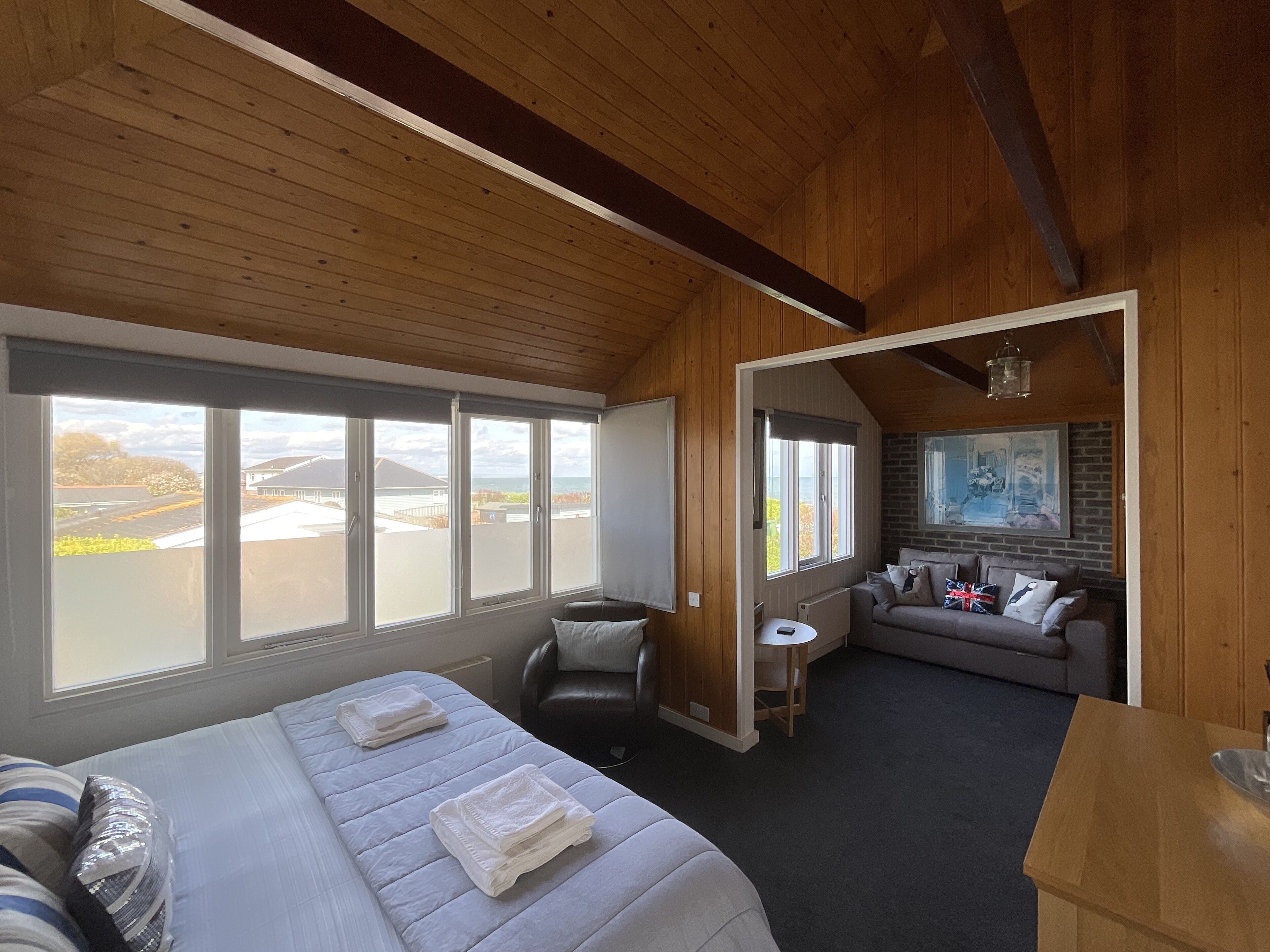 A room with a bed, a sofa, a small table, and a view of the outdoors.
