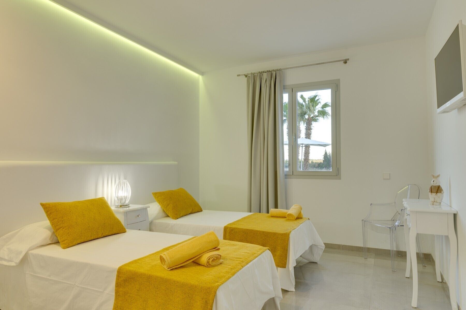 Quarto de hotel com duas camas, uma escrivaninha e uma janela com cortinas.