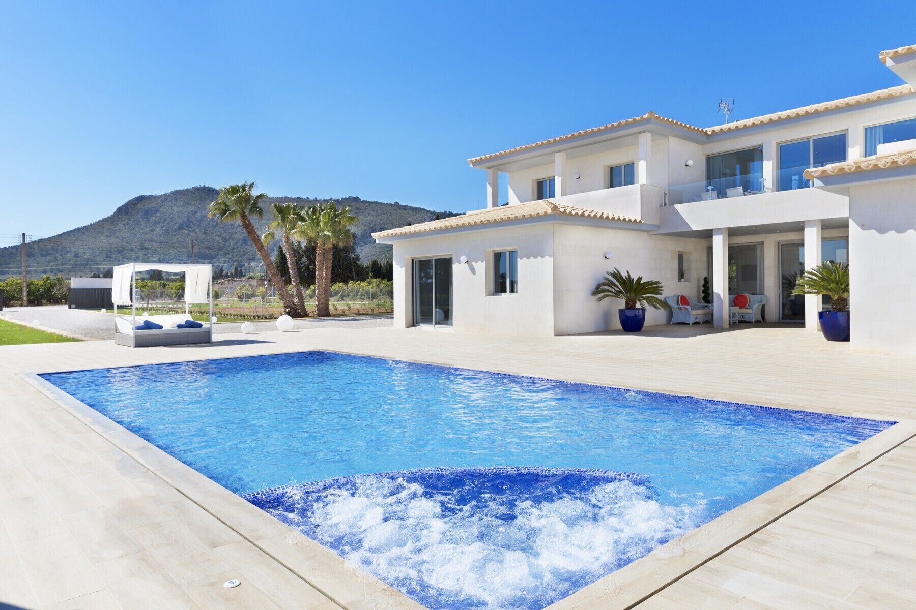 A modern villa with a swimming pool, outdoor seating, and a mountain backdrop.