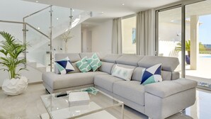 A modern living room with a grey sectional sofa, a glass coffee table, and a staircase with glass railings. - Villa with detached house, air conditioning, wifi, garden, private swimming pool (Inca)