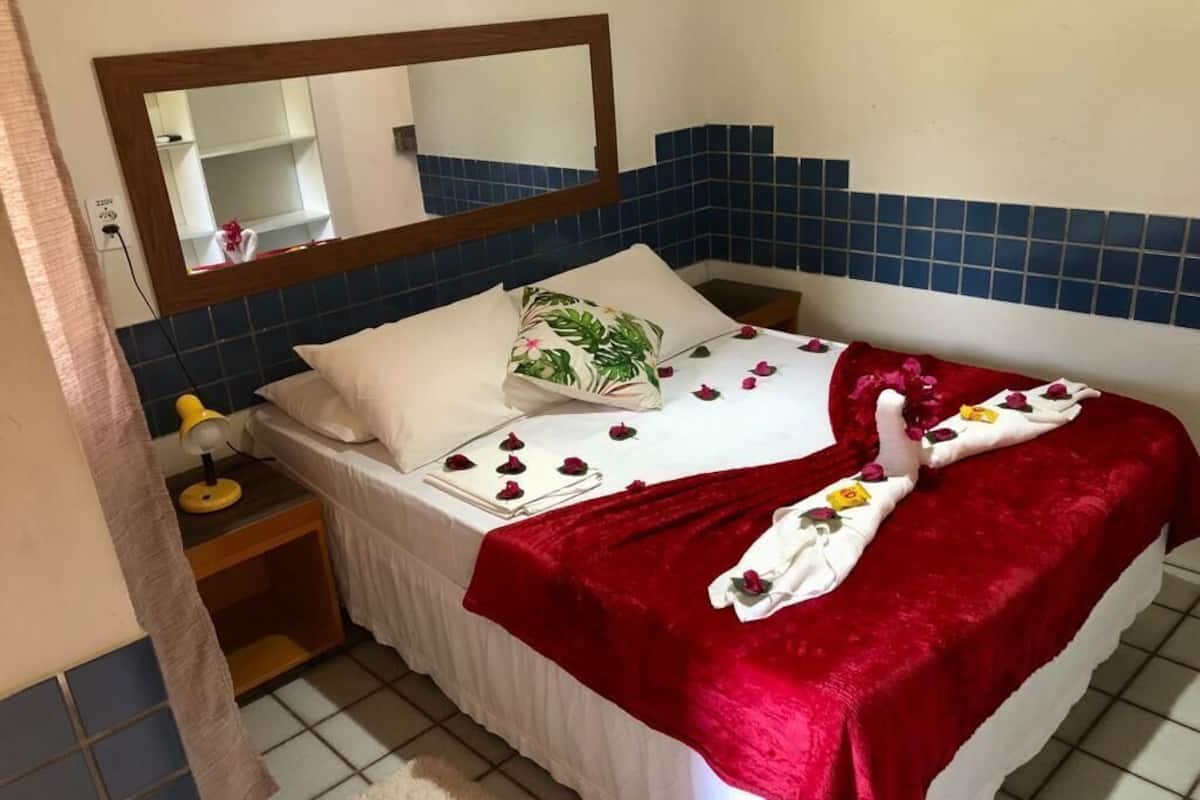 A hotel room with a bed, a nightstand, a mirror, and a red blanket.