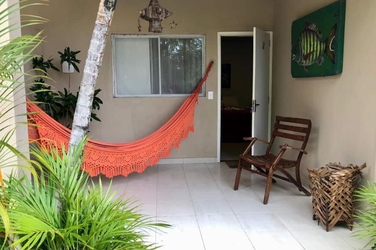 A room with a hammock, a wooden chair, a woven basket, and a fish painting on the wall.