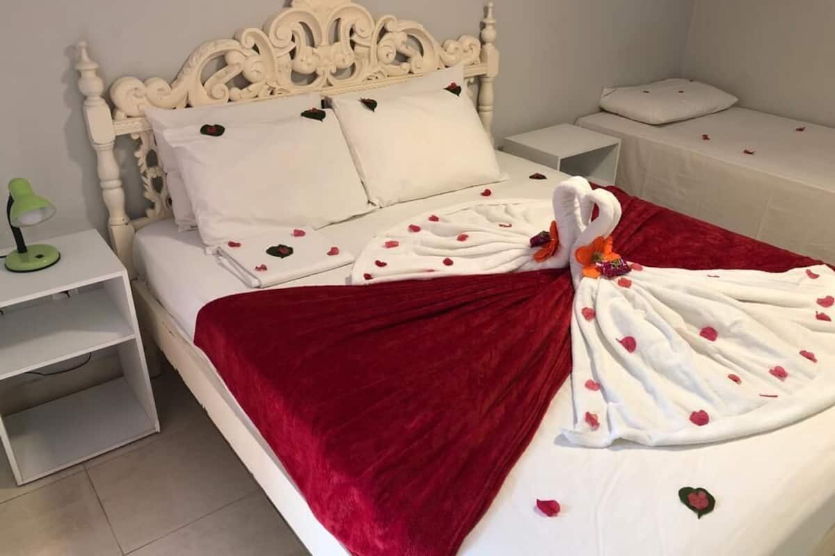 A neatly made bed with a red blanket, white pillows, and a decorative swan towel.
