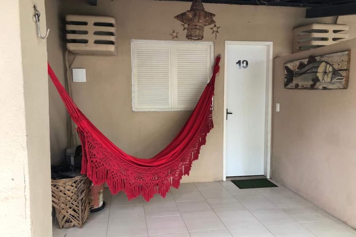 A room with a hammock, a door with the number 19, a window with shutters, and a wall decoration.