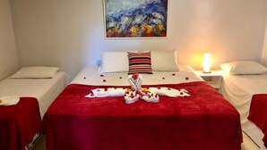 Ein Hotelzimmer mit einem großen Bett, zwei Einzelbetten, einem Gemälde an der Wand und einer roten Decke auf dem Bett.