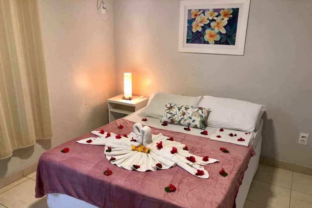 A neatly made bed with a pink bedspread, a decorative towel arrangement, and a bedside lamp.