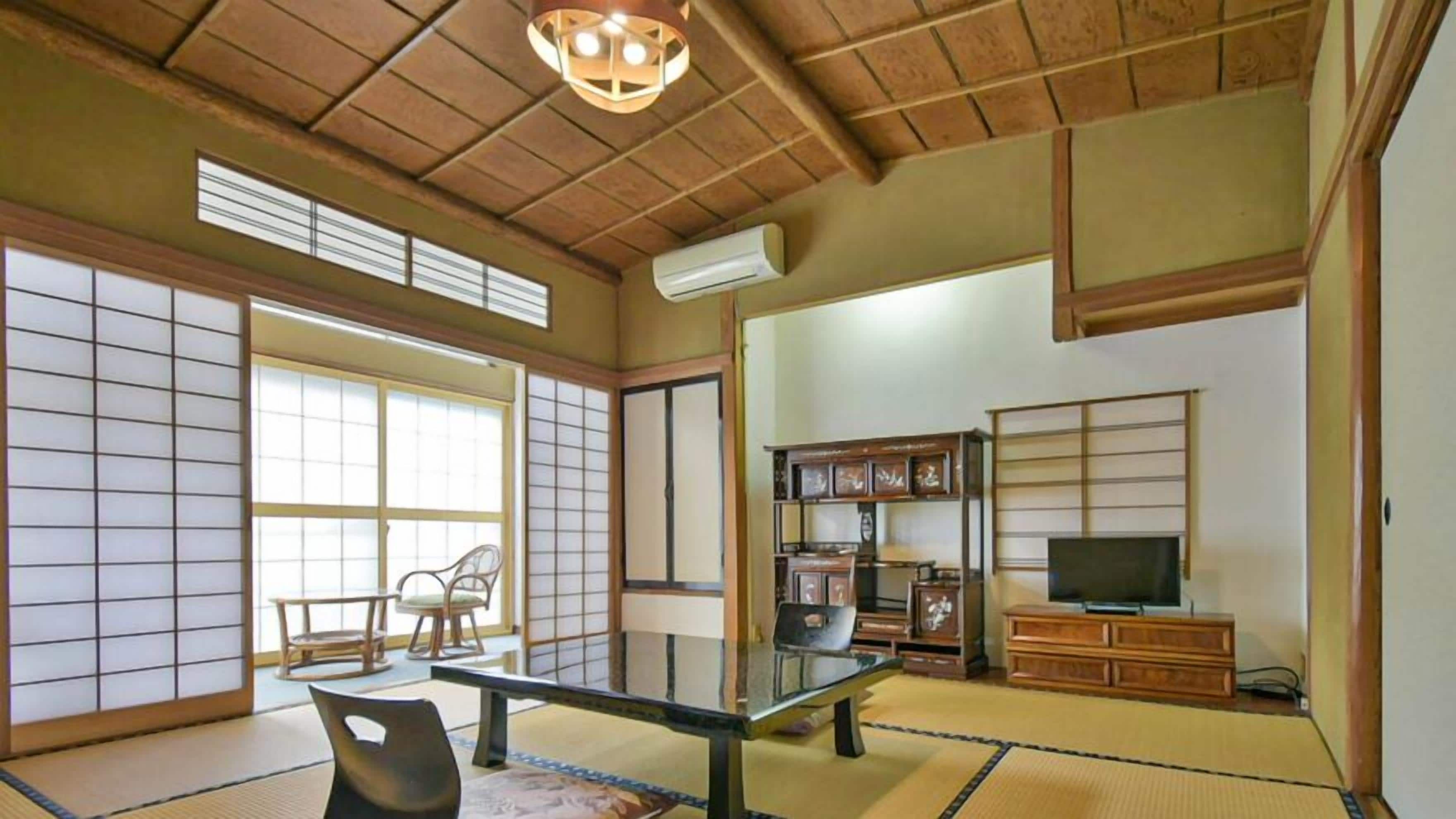 A traditional Japanese room with tatami flooring, a low table, a television, and sliding doors.