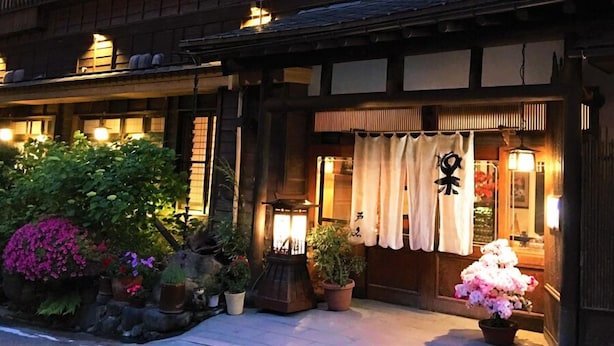 Un bâtiment japonais traditionnel, doté d’une façade en bois, d’une entrée bien éclairée et d’une enseigne avec des caractères japonais.