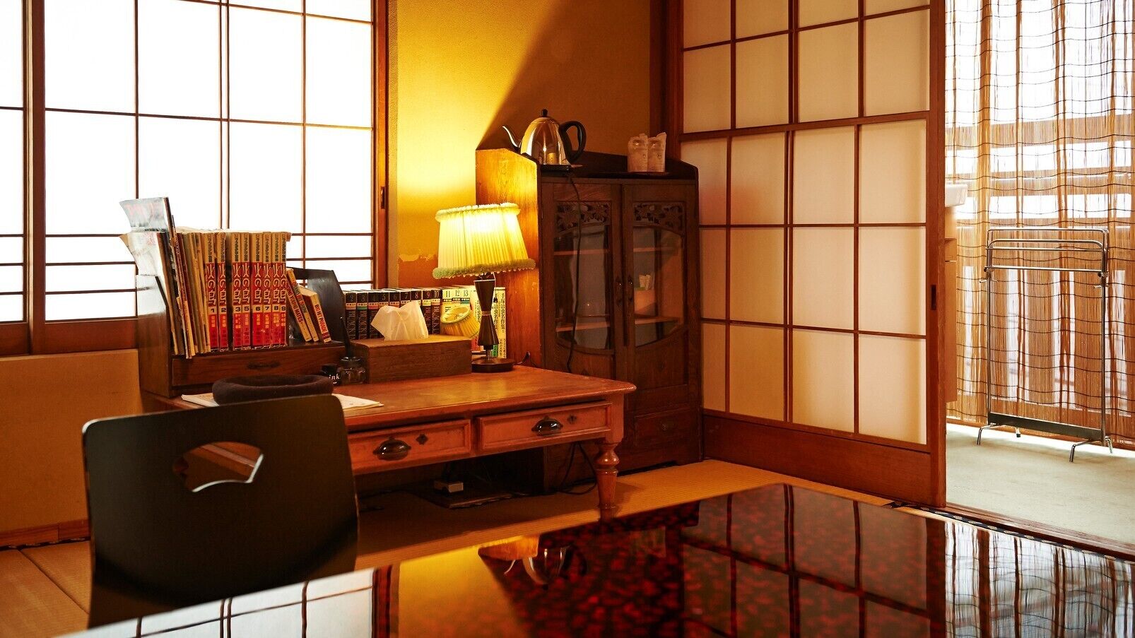 A traditional Japanese room with tatami flooring, a low wooden desk, a lamp, and a bookshelf.
