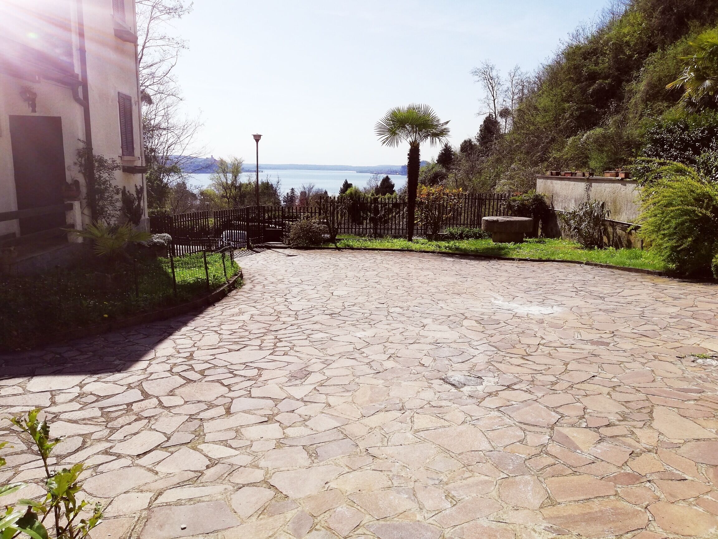Un cortile pavimentato con piastrelle in pietra, una recinzione in metallo e vista sul mare.