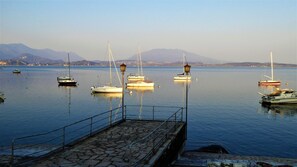 Ein ruhiger Hafen mit mehreren Segelbooten, einer Steinmole und Bergen im Hintergrund.