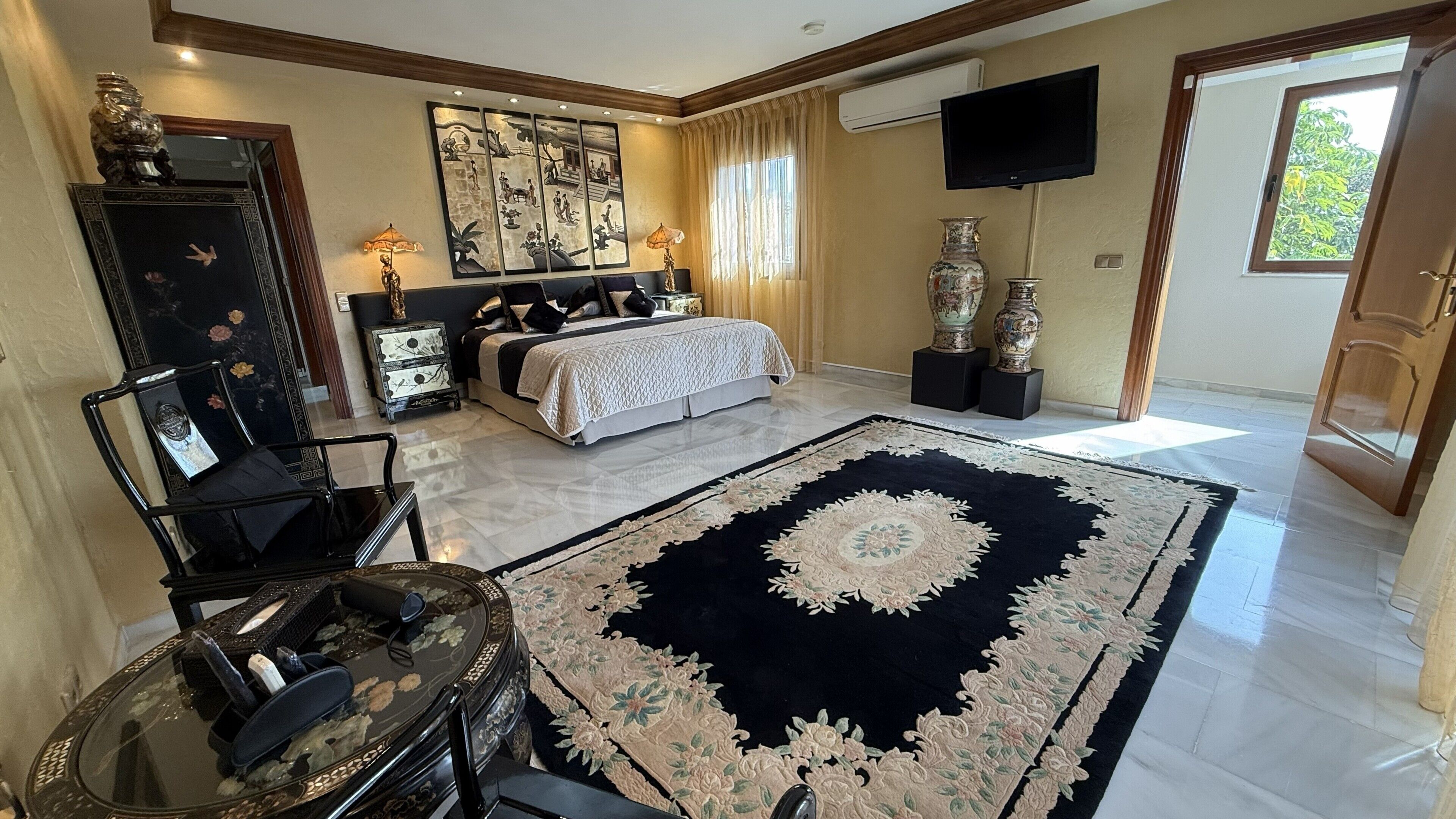 A bedroom with a bed, bedside tables, a large rug, a mirror, a dresser, and a television.
