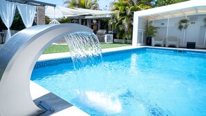 A swimming pool with a water feature, surrounded by outdoor furniture and palm trees. - RENOVATED 2026. BEACHFRONT. 5 MASTER SUITES. HEATED POOL. GAMES ROOM. (Marbella)