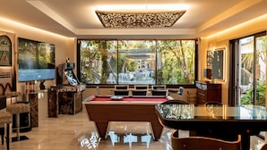 A pool table in a modern room with a large window, a television, and a decorative ceiling panel. - RENOVATED 2026. BEACHFRONT. 5 MASTER SUITES. HEATED POOL. GAMES ROOM. (Marbella)