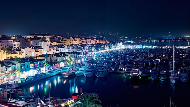 A marina at night with boats docked, buildings along the waterfront, and a cityscape in the background. - RENOVATED 2026. BEACHFRONT. 5 MASTER SUITES. HEATED POOL. GAMES ROOM. (Marbella)