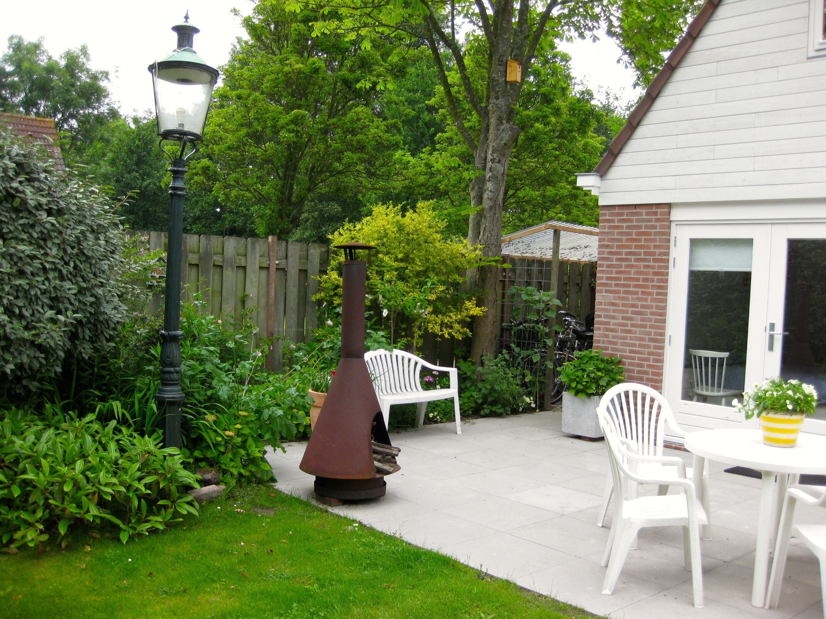 A patio area with a barbecue grill, white chairs, and a table.