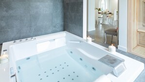 A modern bathroom with a large bathtub, a mirror, and a seating area with a table and chairs.