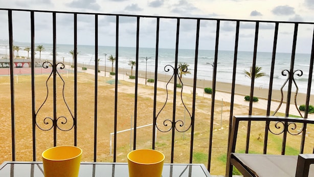A balcony with a view of the beach, two yellow cups on a table, and a chair. - First line of the sea - Port Saplaya (Alboraia)