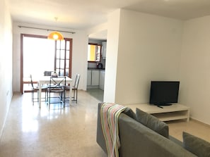 A modern living room with a grey sofa, a flat-screen TV, and a dining area with a table and chairs.