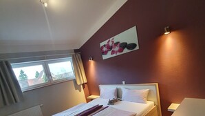 Ein Schlafzimmer mit Bett, Fenster, Heizkörper und einem an der Wand hängenden Bild.