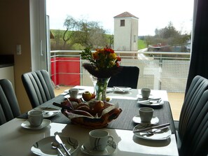 A dining table set with plates, cups, and a basket of pastries, with a vase of flowers in the center.