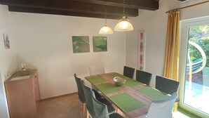 A dining area with a wooden table, green chairs, and a view of the outdoors through a window with curtains. - Beautiful vacation home on the Silbersee with extensive facilities and WLAN (Frielendorf)