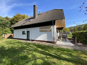 A small, single-story building with a tiled roof and a sign indicating it is a guesthouse named "Feriendomizil am Silbersee."