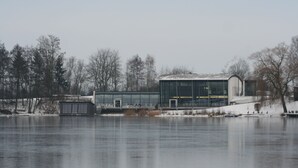 A building with a glass facade near a body of water, surrounded by trees and snow. - Beautiful vacation home on the Silbersee with extensive facilities and WLAN (Frielendorf)
