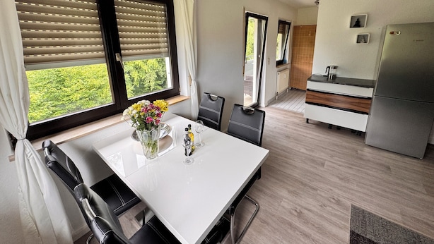 A modern kitchen with a dining area, large windows with blinds, a refrigerator, and a sink. - Idyllic apartment in Friedrichshafen / Manzell NEW !!!! (Friedrichshafen)