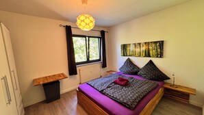 A bedroom with a bed, a window with curtains, a radiator, a wall-mounted artwork, and a bedside table. - Idyllic apartment in Friedrichshafen / Manzell NEW !!!! (Friedrichshafen)
