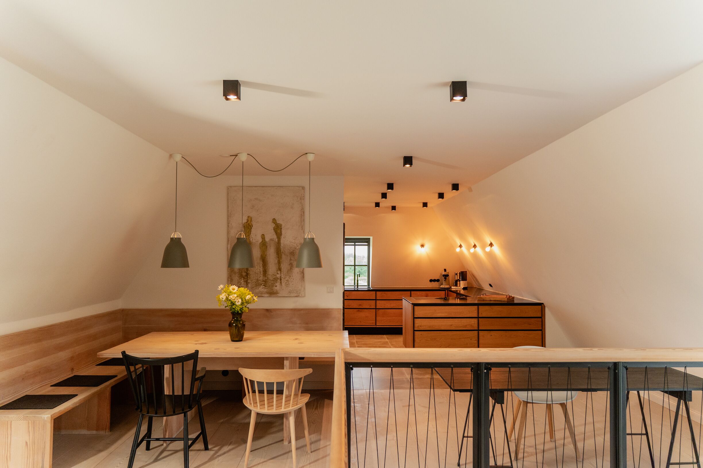 Une cuisine moderne avec des meubles en bois, un coin repas comprenant un banc et des chaises, et un éclairage suspendu.