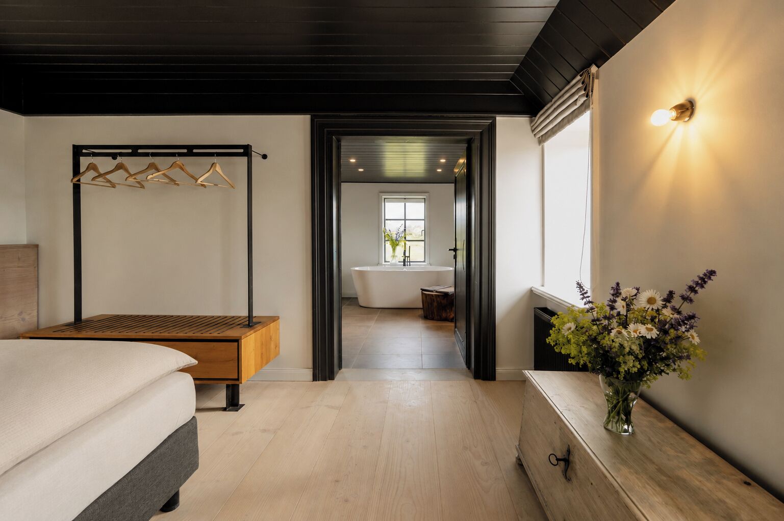 A modern bedroom with a wooden bed, a bedside table, and a hanging clothes rack.
