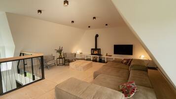 A modern loft-style living room with a large sofa, a fireplace, and a flat-screen TV mounted on the wall.