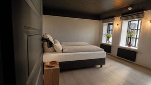 A bedroom with a bed, bedside tables, a wooden floor, and a window with plants. - Rickmer’s Hoff Cottage| Sauna, Kamin & Weitblick (Pellworm)