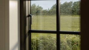 A window with a view of a grassy field and trees. - Rickmer’s Hoff Cottage| Sauna, Kamin & Weitblick (Pellworm)