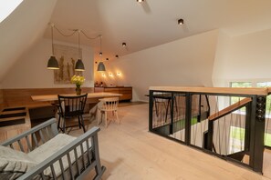 Una habitación moderna estilo loft con una mesa de comedor de madera, sillas, un sofá y una escalera con barandillas de vidrio.