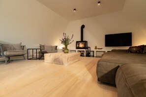 Una sala de estar moderna con piso de madera, un sofá, una mesa de centro, un televisor montado en la pared y una chimenea a leña.
